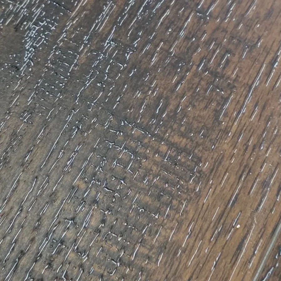 Close-up of drywall compound packed into the embossed wood-grain texture of luxury vinyl plank, with the trowel pattern visible