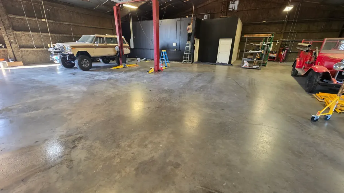 Before: a bare concrete shop floor in Houston with a gray grime film and oil stains around a two-post lift